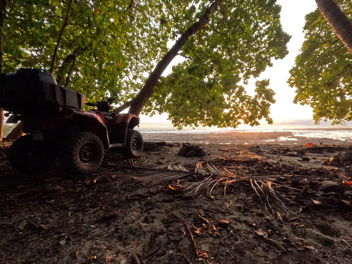 A red 4x4 quad with a cargo box parked under the trees at Mar Azul beach at sunset