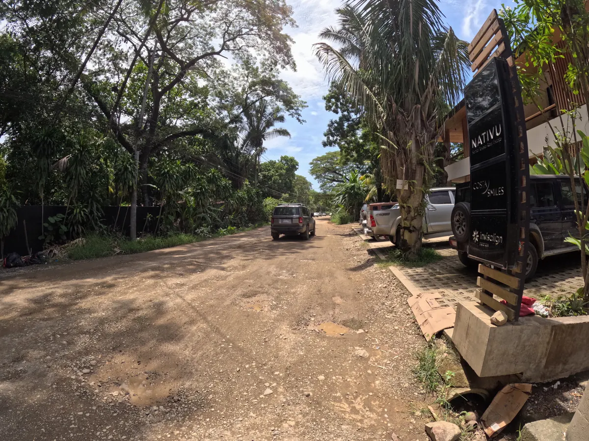 An unpaved side road in Santa Teresa with potholes and SUVs parked along the edge