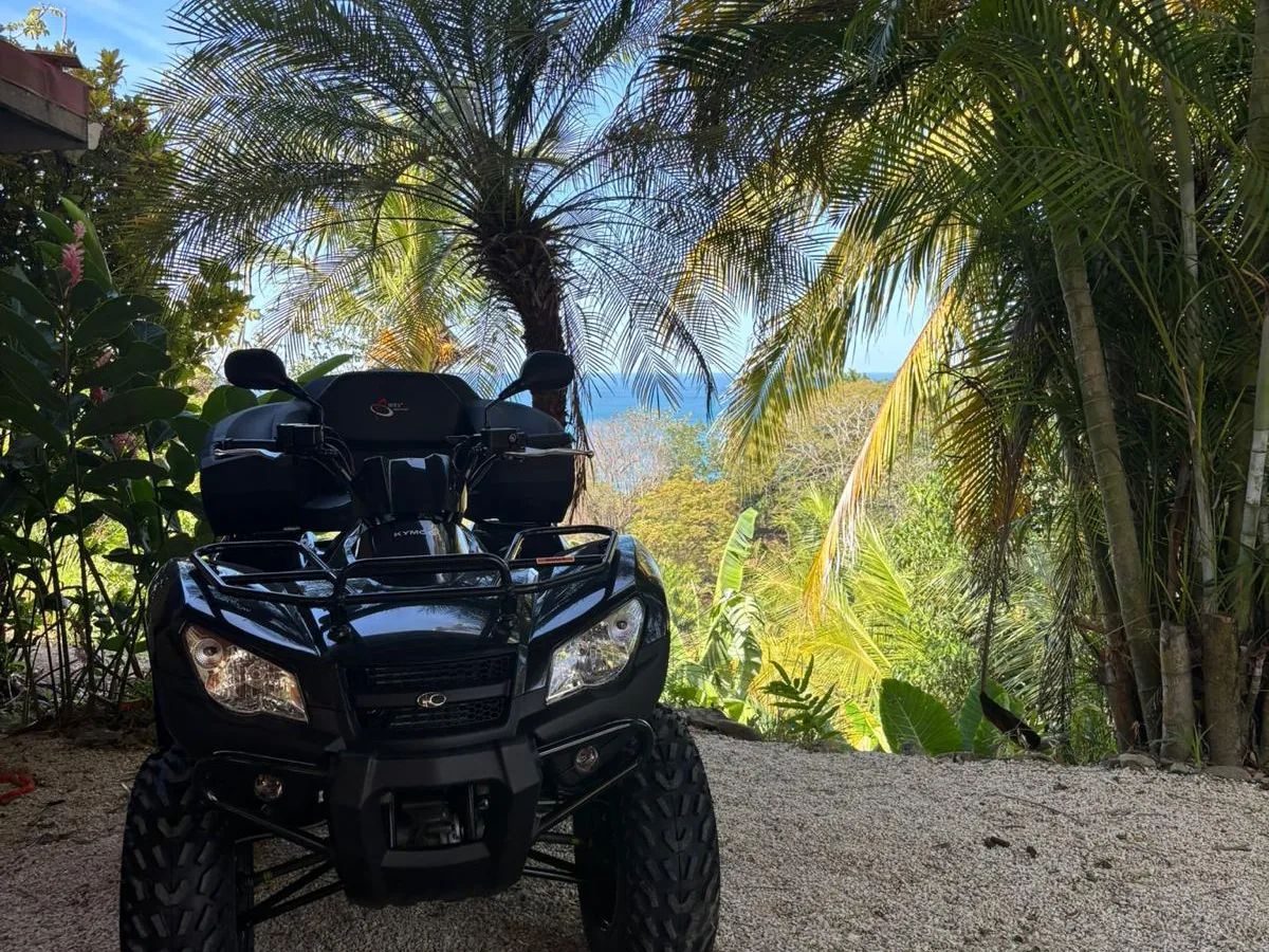 Black Kymco ATV parked with an ocean view over the jungle